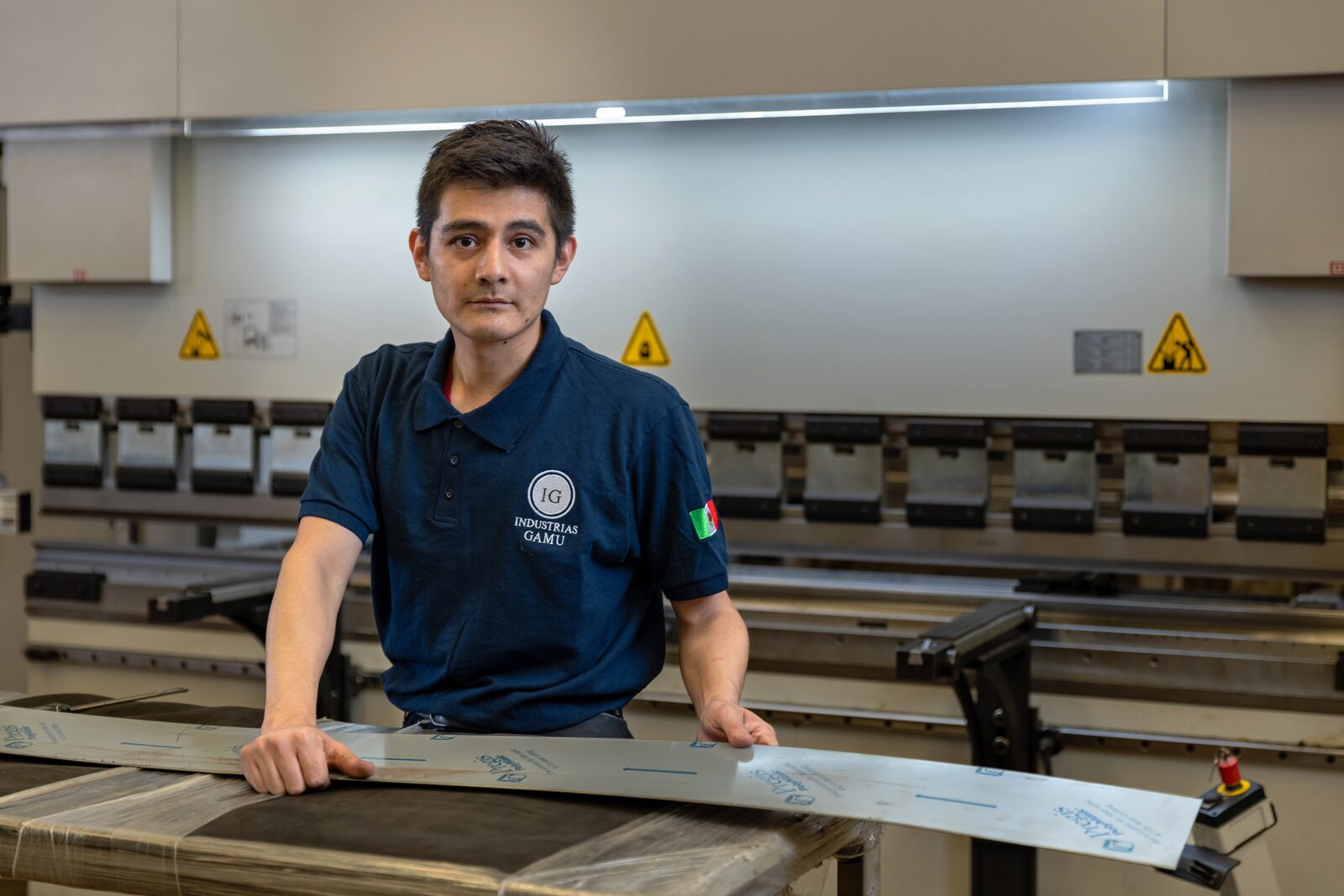 Operador de GAMU sosteniendo una lámina larga frente a la plegadora CNC