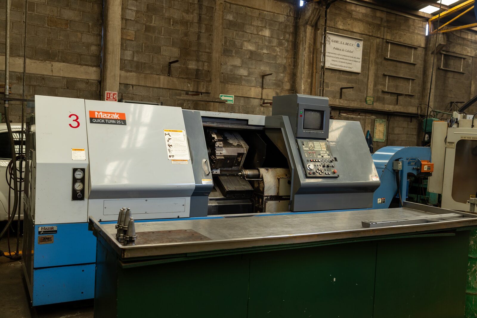 Torno CNC Mazak Quick Turn 25L (nº 3) completo; política de calidad GAMU S.A. de C.V. en el muro.