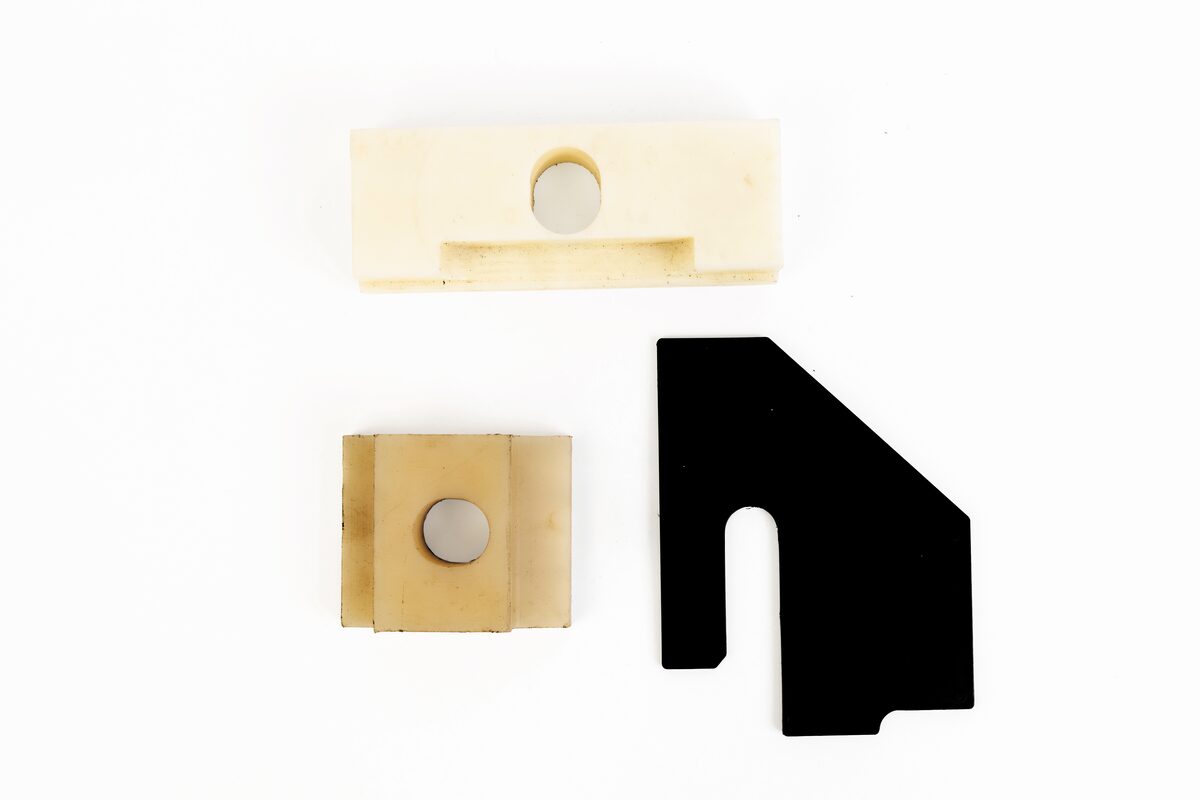 Tres bloques aislantes maquinados en nylon color hueso y una placa negra en L.